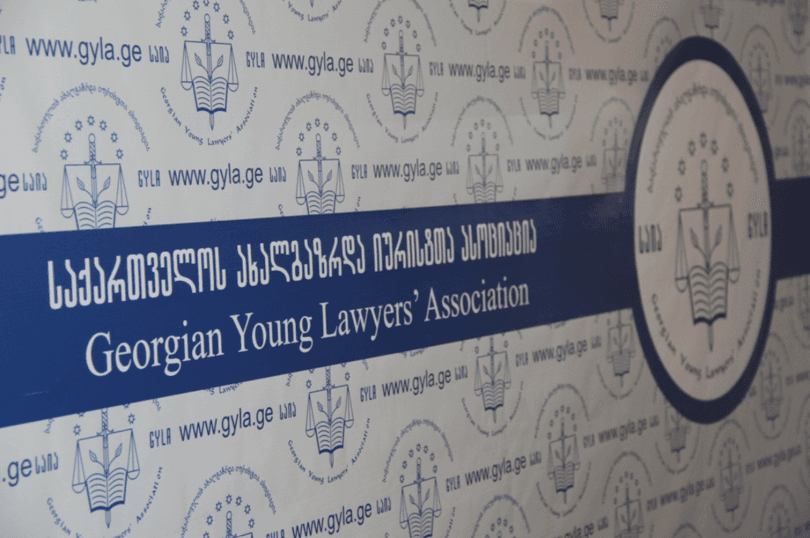 საქართველოს ახალგაზრდა იურისტთა ასოციაციის ლოგო და პოლიციის შენობის ფოტო
